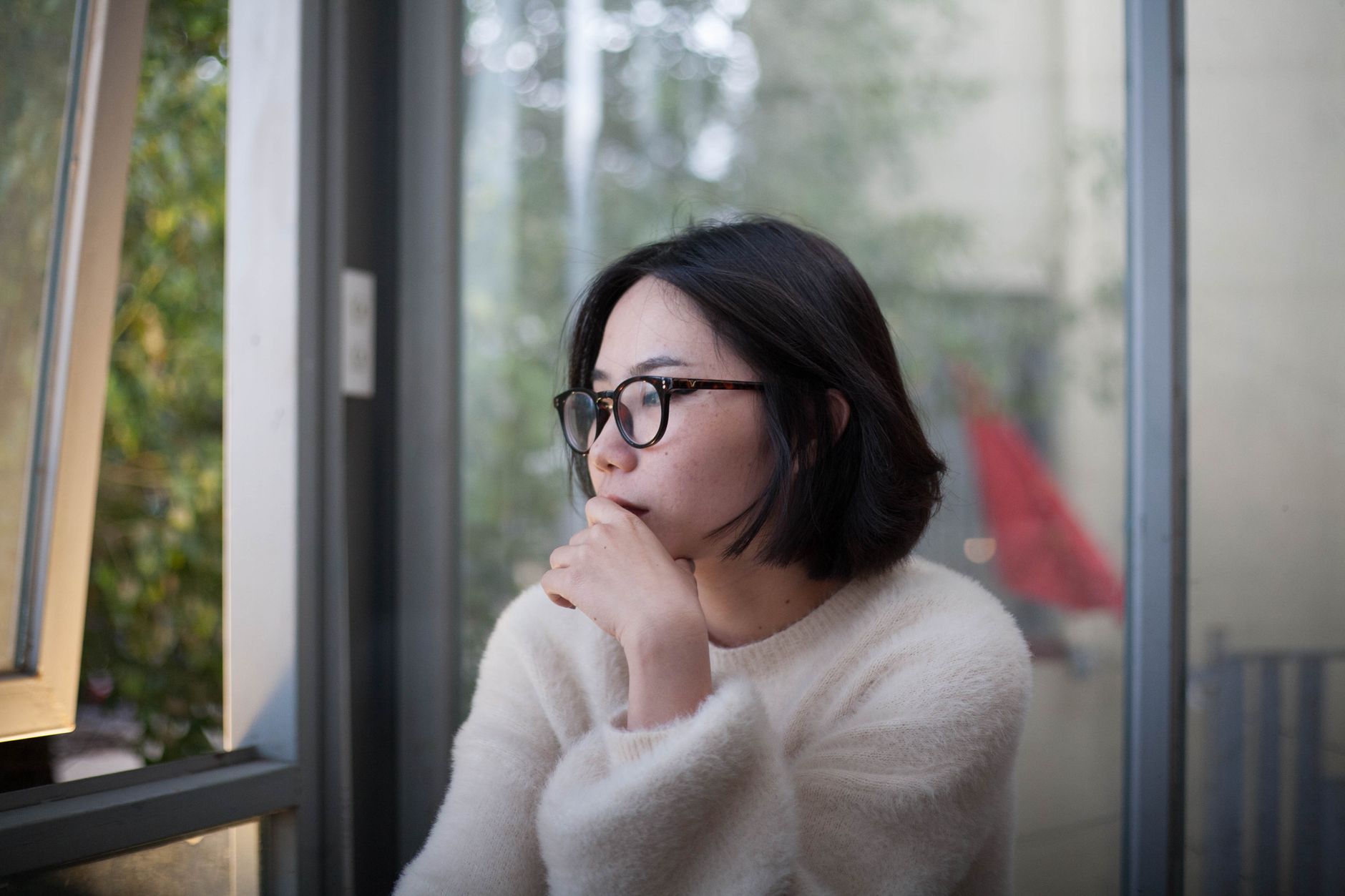 Mujer pensativa mirando por la ventana, reflexionando sobre sus finanzas.